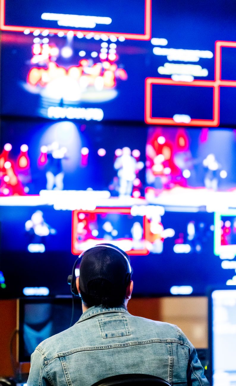 Technician with headphones monitoring live video feeds on multiple screens.