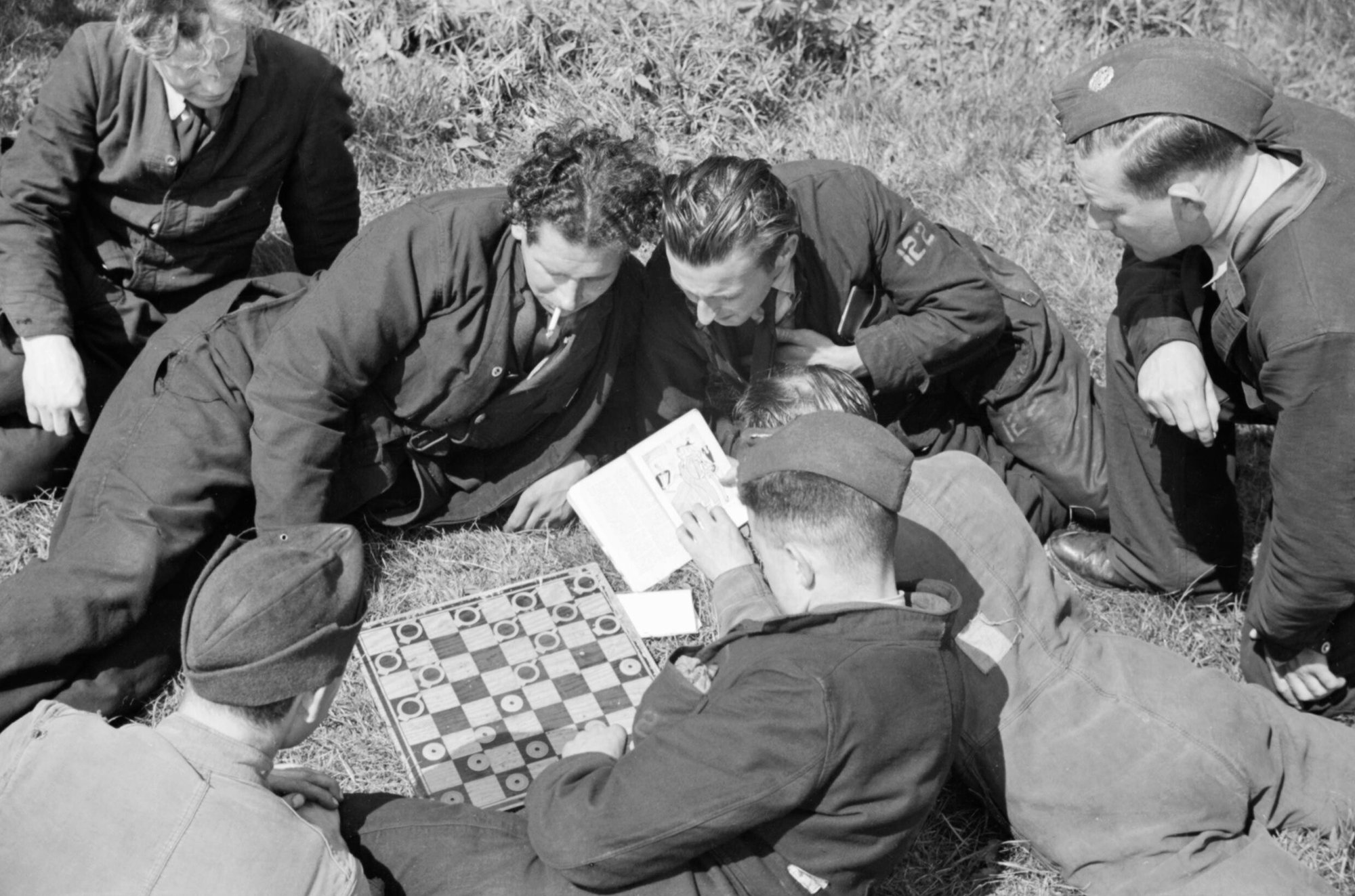 Groundcrew from No. 122 Squadron RAF play a game of draughts while waiting for their aircraft to return from an operation over France, Hornchurch, 7 May 1942. This image is part of a sequence of five photographs taken on 7 May 1942 at Hornchurch, and later released by the Ministry of Information to illustrate a typical offensive operation. In this photograph we see members of No 122 Squadron while away the time with a game of draughts - using washers and circlips as playing pieces - as they return for the Spitfires on operation to return.